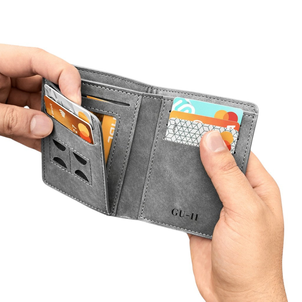 A gray textured leather bifold wallet being held open by two hands, showing card slots, ID window cutouts, and an embossed 'GU-II' logo on the inside.